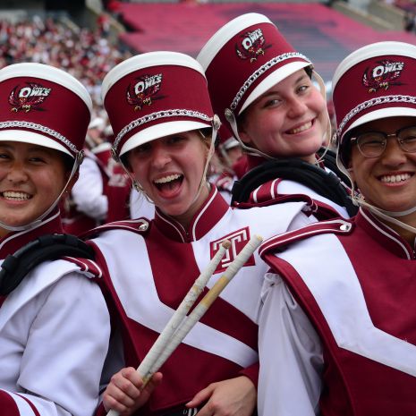 Four smiling marching band members in cherry and white uniforms
