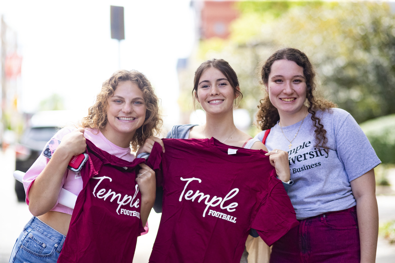 Three students holding up red Temple t shirts