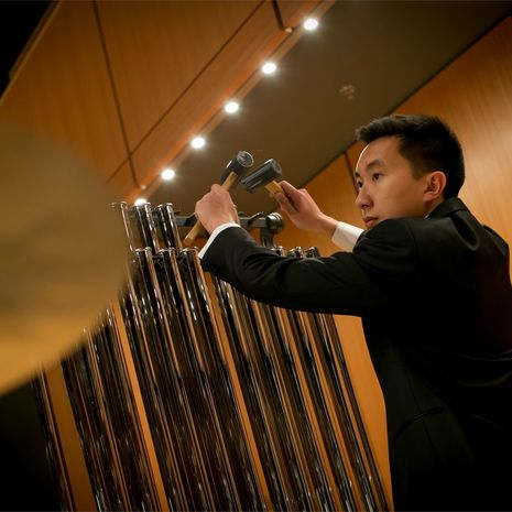 A student plays symphonic chimes as part of an orchestra performance.